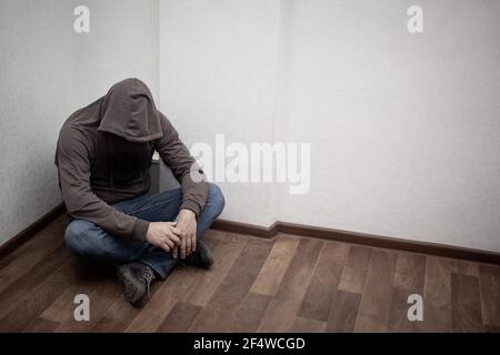 desperate young drug addict wearing hood and sitting alone in corner. concept of sadness, depressed and life problems Stock Photo