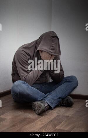 desperate young drug addict wearing hood and sitting alone in corner. concept of sadness, depressed and life problems Stock Photo