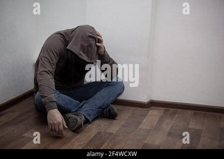 desperate young drug addict wearing hood and sitting alone in corner. concept of sadness, depressed and life problems Stock Photo