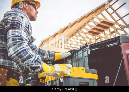 Contractor Worker Preparing Himself For Another Day in Construction Job Checking His Tools Boxes in Front of the Structure. Stock Photo
