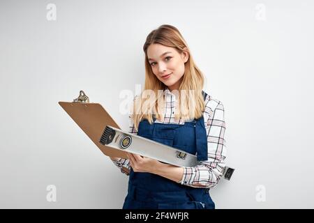 Engineer female in builder uniform smile, hold business paper and level tool in hands, look at camera isolated over white studio background. portrait Stock Photo