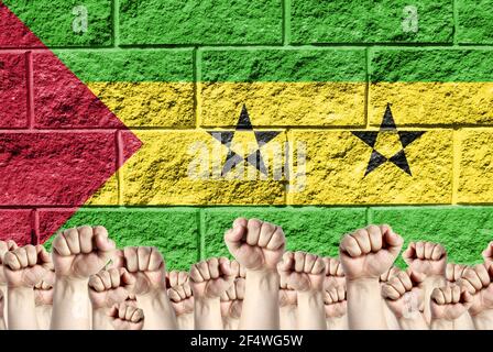 Raised fists against the background of the depicted flag of Sao Tome and Principe on a brick wall, a concept of strength and unity. Stock Photo