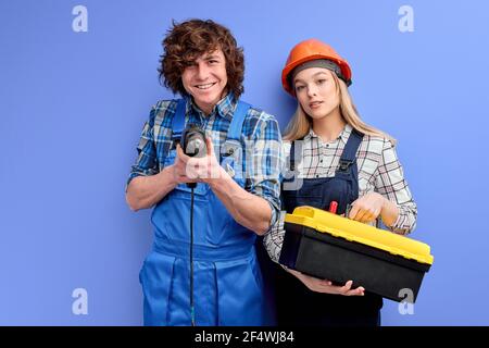 team of friendly positive constructors with instruments tools posing isolated on blue background, two architects co-workers standing together looking Stock Photo