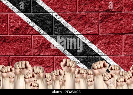Raised fists against the background of the depicted flag of Trinidad and Tobago on a brick wall, a concept of strength and unity. Stock Photo