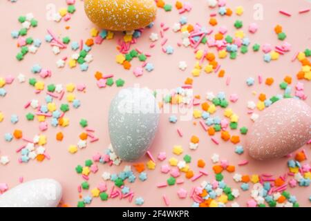 White, grey and yellow eggs on pink background with colourful sprinkles. Easter holiday background. Stock Photo
