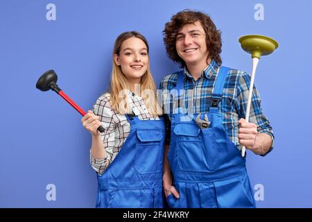 Positive team of two plumbers dressed in blue uniform with plunger, being glad to repair bathtub, recieve pleasant comments from clients, isolated ove Stock Photo