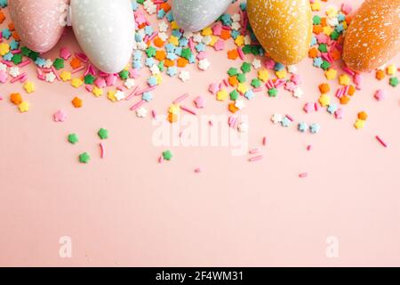 White, grey and yellow eggs on pink background with colourful sprinkles. Easter holiday background. Stock Photo
