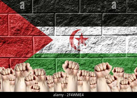 Raised fists against the background of the depicted flag of Western Sahara on a brick wall, a concept of strength and unity. Stock Photo