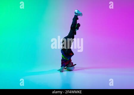 Beautiful sportive boy dancing hip-hop in stylish clothes on colorful gradient background at dance hall in neon light. Stock Photo