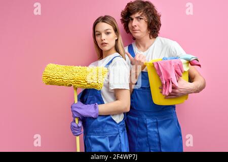 Couple cleaning , doing housework household chores together, using rags. caucasian man and woman posing isolated over pink studio background, wearing Stock Photo