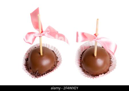 Two delicious chocolate glazed candies on stick with pink silk ribbon. Macro. Selective focus on candies. Isolated on a white background. Stock Photo
