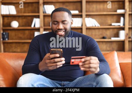 Online transaction, payment. African-american man holding credit card and using smartphone for shopping, a dark skinned guy with mobile phone and making purchases online Stock Photo