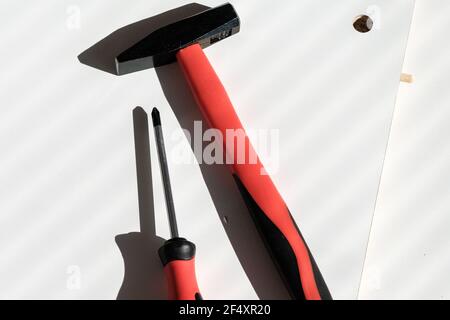 A hammer and a screwdriver on a white wooden surface. Red handles tools Stock Photo
