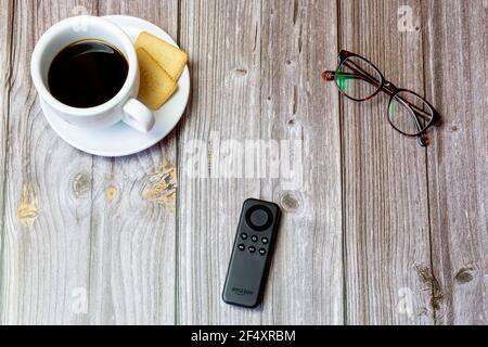 An Amazon fire stick remote control laid on a wooden table next to a coffee and glasses Stock Photo