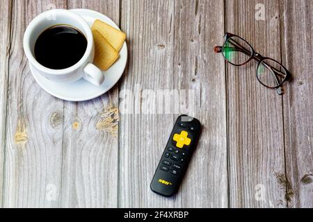 A Now TV Remote control laid on a wooden table next to a coffee and a pair of glasses Stock Photo