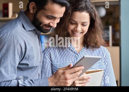Smiling indian and latin colleagues talking using digital tablet in office. Stock Photo