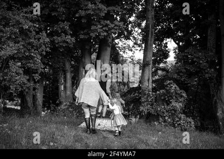 Parents holding hands with daughters walking on path through trees Stock Photo
