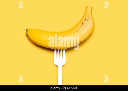 Banana on a white plastic fork on a yellow background.Healthy food lifestyle Stock Photo