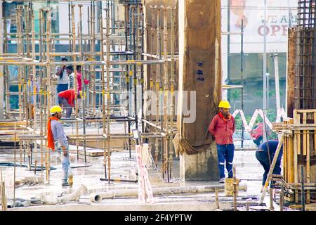 construction site in india at dusk with workers, people, labor, engineers in colorful clothes among rebar wood concrete pillars working Stock Photo