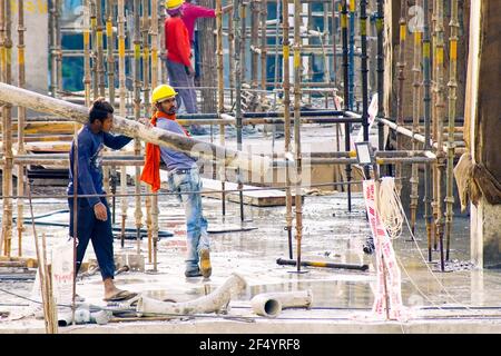 construction site in india at dusk with workers, people, labor, engineers in colorful clothes among rebar wood concrete pillars working and carrying a Stock Photo