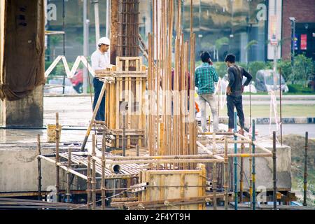 construction site in india at dusk with workers, people, labor, engineers in colorful clothes among rebar wood concrete pillars working Stock Photo