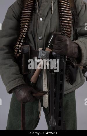 actor man in the old winter mountain uniform near the MG 42 machine gun during the World War II posing on a gray background Stock Photo