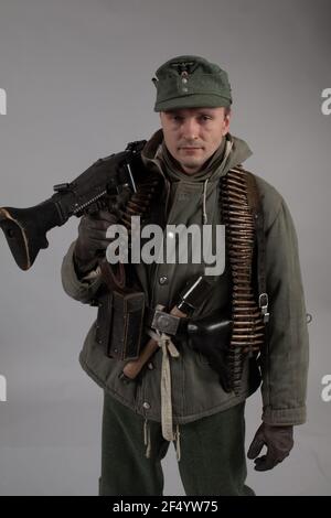 actor man in the old winter mountain uniform near the MG 42 machine gun during the World War II posing on a gray background Stock Photo