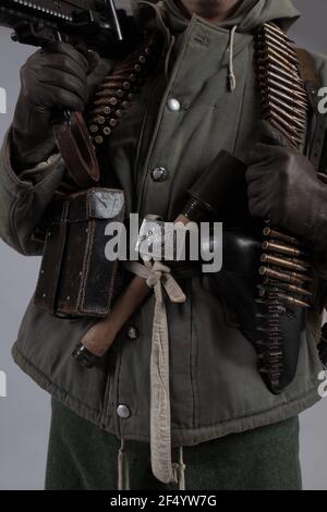 actor man in the old winter mountain uniform near the MG 42 machine gun during the World War II posing on a gray background Stock Photo