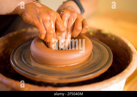 Hands of potte makes pottery dishes on potter's wheel. Sculptor in workshop makes clay product closeup Stock Photo