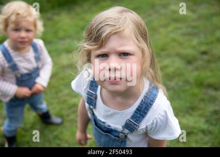 Portrait serious blonde girl in overalls with sister Stock Photo