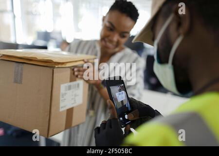 Courier in face mask with smart phone scanning package in office Stock Photo