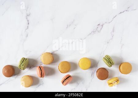 Multi colored french macaroons top view on white marble table. French meringue cookie macarons background. Stock Photo