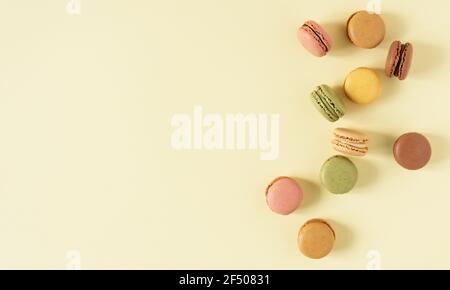 Multi colored french macaroons top view on yellow pastel background. French meringue cookie macarons. Stock Photo