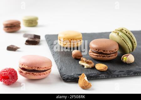 Variety of french macaroons with raspberry, nuts and chocolate on white wooden table. French meringue cookie macarons. Stock Photo
