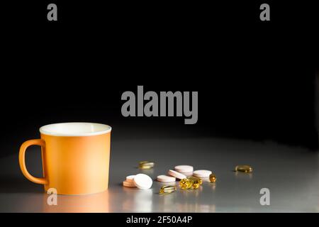 Orange ceramic mug on a gray table on a black background with omega-3 capsules and effervescent tablets with vitamins. Food supplements, vitamins. Stock Photo
