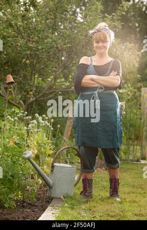 Portrait confident woman with watering can in summer garden Stock Photo