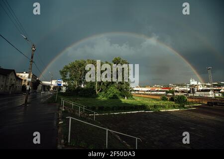 rainbow in the sky over the city after the rain. an old steam locomotive stands at the railway station Stock Photo