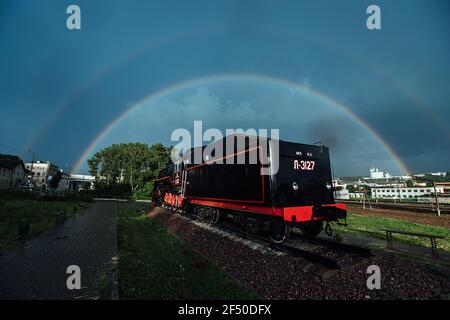 rainbow in the sky over the city after the rain. an old steam locomotive stands at the railway station Stock Photo