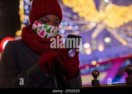 Young woman in Christmas face mask and scarf using smart phone Stock Photo