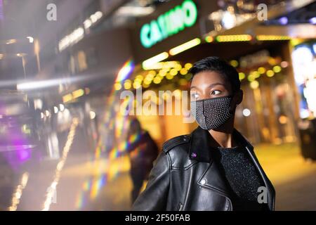 Young woman in studded face mask on city street at night Stock Photo