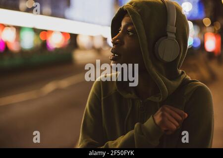 Young woman in hoody with headphones on city street at night Stock Photo