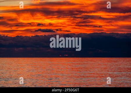 Glorious sunset over the sea with dark clouds on the horizon and red reflections on the rippling water Stock Photo