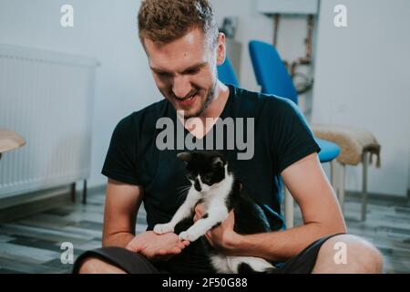 Young blonde caucasian male playing with his cat at home Stock Photo