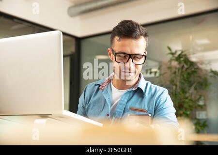 Businessman using smart phone at laptop in office Stock Photo