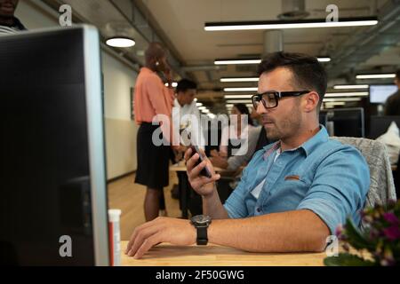 Businessman using smart phone at computer in open plan office Stock Photo