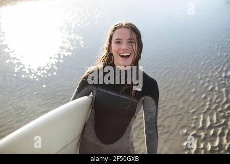 Portrait happy young female surfer in wet suit with surfboard on beach Stock Photo
