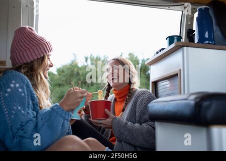 Happy young women friends eating instant noodles in camper van Stock Photo