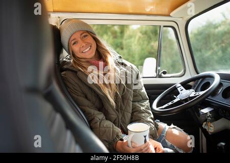 Portrait happy young woman drinking coffee at steering wheel in van