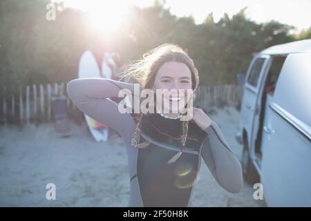 Portrait happy young female surfer in wet suit outside sunny van Stock Photo
