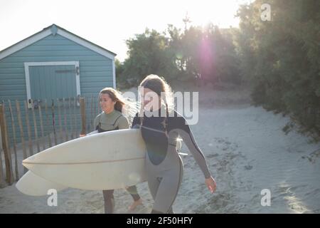 Young female surfers walking with surfboards on sunny beach path Stock Photo